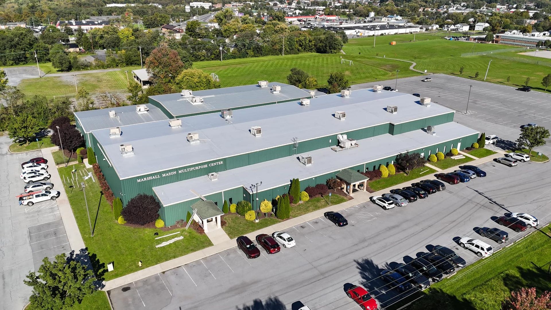 Aerial view of a light gray single ply membrane roof on the Marshall Mason Multipurpose Center, a large commercial building with green metal walls and rooftop HVAC units, in the Martinsburg WV area