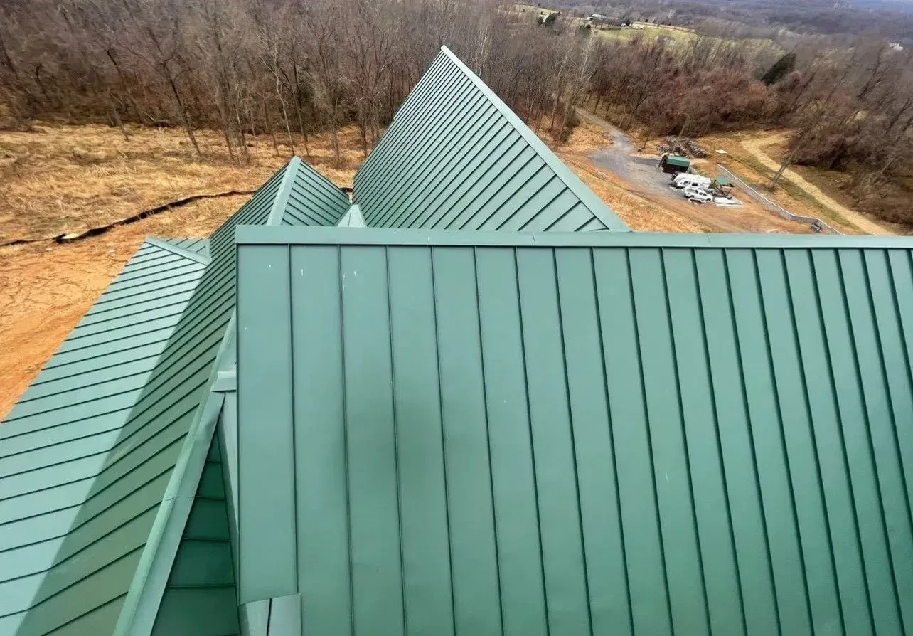 Close up of a finished sage green standing seam metal roof with steep gables and clean vertical seams on a rural hillside property served by Black Stone Roofing near Martinsburg WV